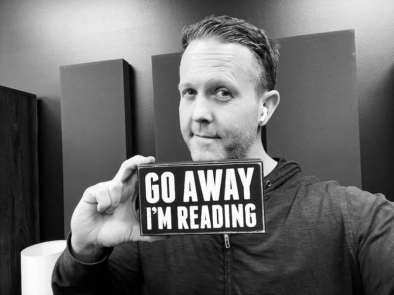 A man holding a sign that says "Go Away, I'm Reading."
