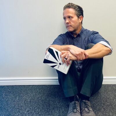 A man sitting against a wall with a book.