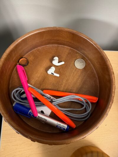 AirPods in a bowl on a desk.