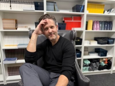 A man on a chair in front of a bookcase.