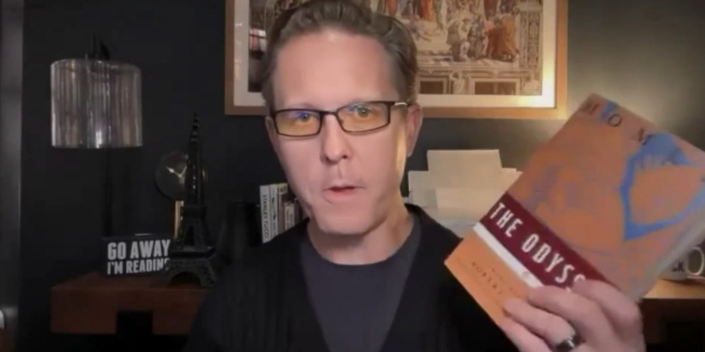 A speaker holding up The Odyssey during a recorded Read Well Book Club session